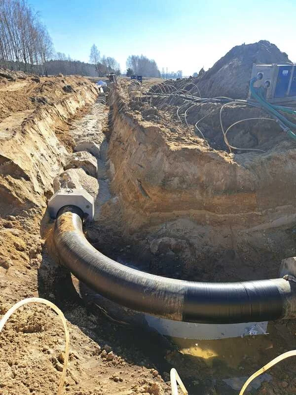 Precyzyjny montaż niebieskiej armatury gazowej i zaworów na stalowym rurociągu w zabezpieczonym wykopie betonowym.